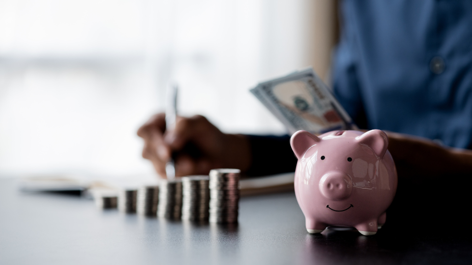 Personne comptant de l’argent avec une pile de pièces de monnaie et une tirelire